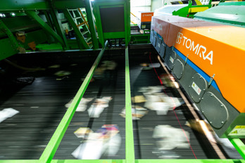 The interior of the Re-Gen recycling plant shows a close-up shot of a conveyor belt that has recycling items passing at speed underneath. An infra-red scanner is helping to sort the materials as they pass beneath.