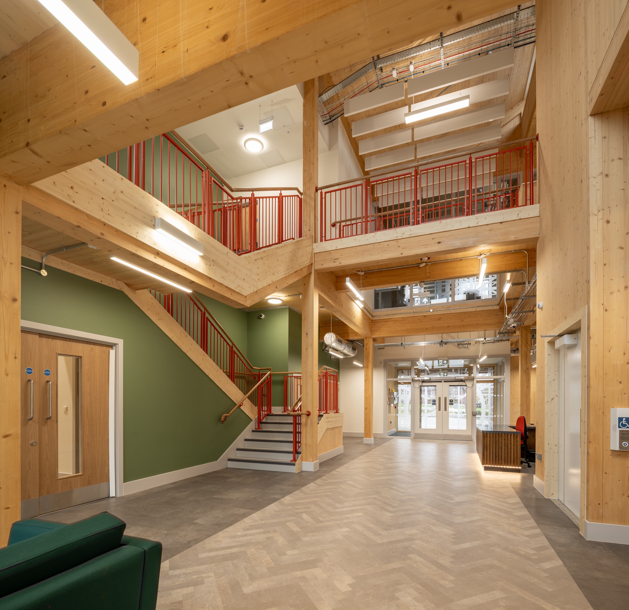 Light-filled atrium at Northstowe Unity Centre with timber structure, red railings, stairs and reception area.